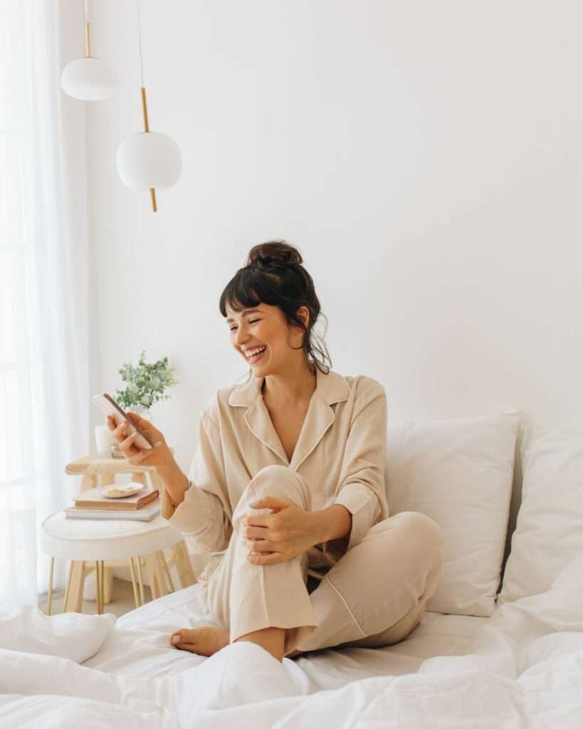 femme en pyjama souriante sur son téléphone avec applications écogestes