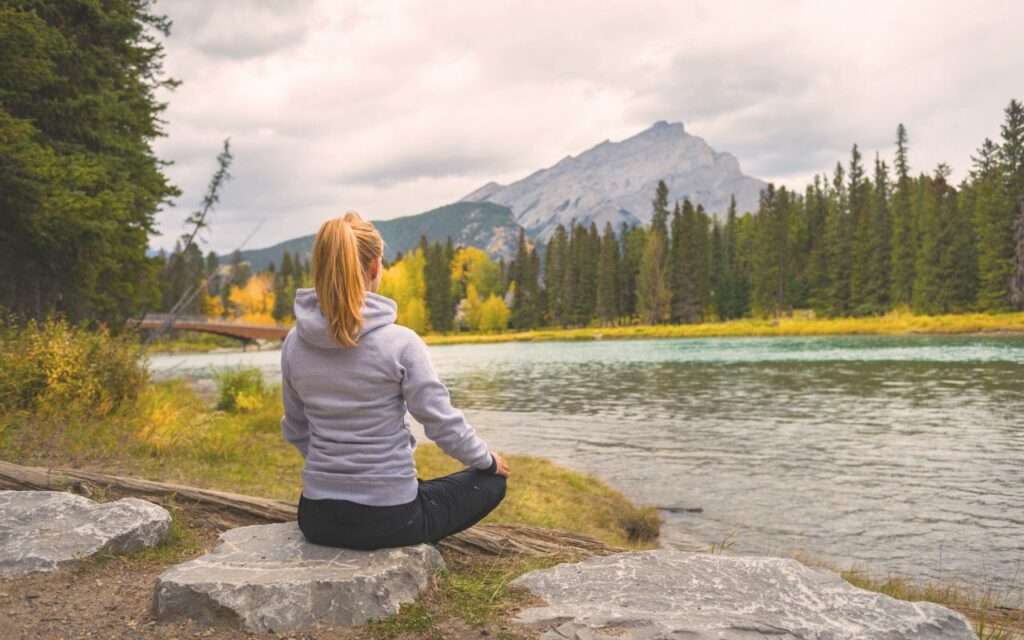 femme assise au bord d'une rivière dans la nature.