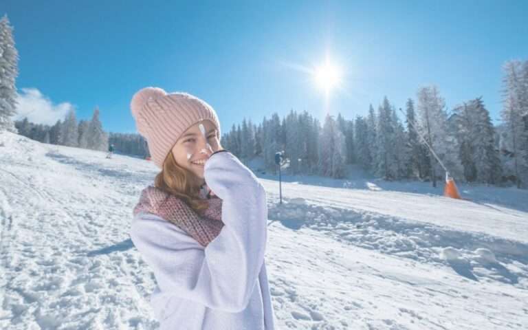 fille avec bonnet rose sur une piste de ski et crème solaire sur le visage